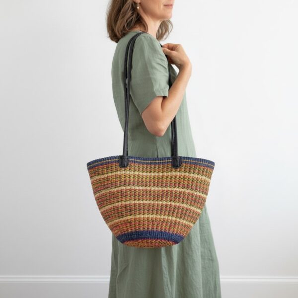Hand-bag-188-static (1)-bashiri-shoulder-bag Model carrying a handmade Bolga shoulder bag featuring leather straps, tassel and woven striped design.