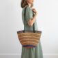 Model carrying a handmade Bolga shoulder bag featuring leather straps, tassel and woven striped design.