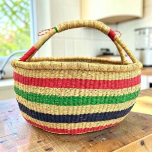 large round woven basket with vegan handle and green, pink, and black stripes.