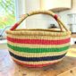 large round woven basket with vegan handle and green, pink, and black stripes.