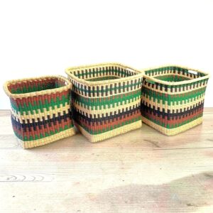 Three Ago square baskets with a green, brown and black stepped pattern sitting side by side on a pale timber floor.