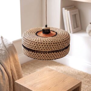 Woven bolga lampshade hanging in a bedroom, natural straw with a rust-orange centre and black base band