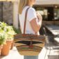 Bolga shoulder bag in natural straw , leather handles and tassel, worn over shoulder outdoors.