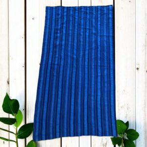 Indigo cotton cloth in mid and deep blue stripes, laid flat on a timber floor beside a plant