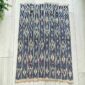 Indigo cotton cloth with columns of pale diamond motifs, laid flat on a timber floor beside a plant