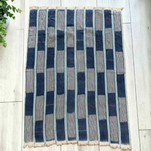 Indigo cotton cloth with solid and pinstriped panels, laid flat on a timber floor beside a plant