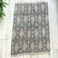 Faded indigo cotton cloth with pale diamond lattice motifs, laid flat on a timber floor beside a plant