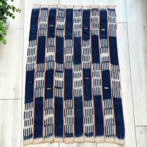 Deep indigo cotton cloth with pale striped bands, laid flat on a timber floor beside a plant