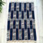 Deep indigo cotton cloth with pale striped bands, laid flat on a timber floor beside a plant