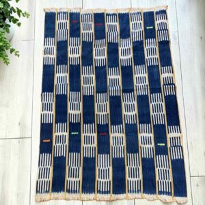 Indigo cotton cloth in a checkerboard of deep and pale blocks, laid flat on a timber floor beside a plant