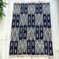 Dark indigo cotton cloth with pale zigzag and window motifs, laid flat on a timber floor beside a plant