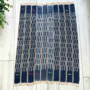 Deep blue cotton cloth with columns of pale dashes, laid flat on a timber floor beside a plant