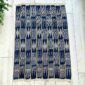 Dark indigo cotton cloth with pale arrow and zigzag motifs, laid flat on a timber floor beside a plant