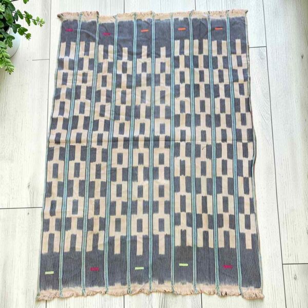 bashiri-indigo-cotton-242-keta-handwoven-african-textile-main Pale cotton cloth with a stepped pattern of indigo blocks, laid flat on a timber floor beside a plant