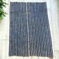 Cotton cloth with fine indigo and pale stripes, laid flat on a timber floor beside a plant