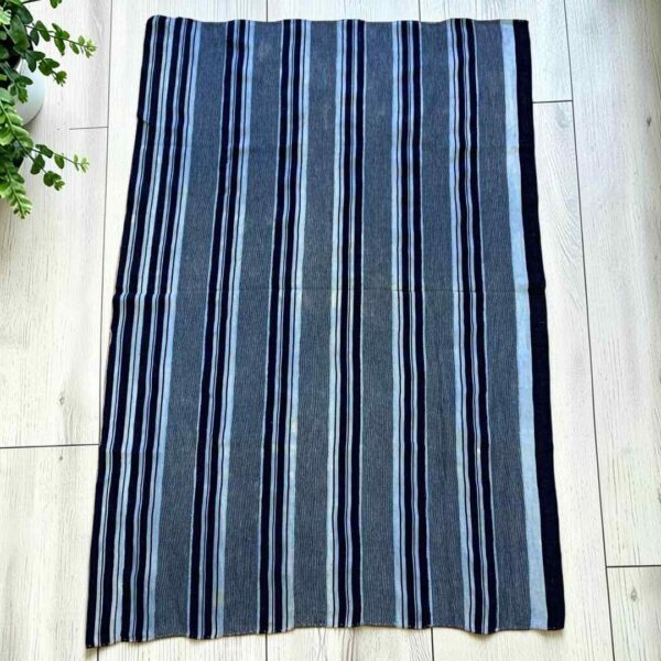 bashiri-indigo-cotton-244-akosombo-african-textile-handwoven-main Grey-blue cotton cloth with bands of dark and pale stripes, laid flat on a timber floor beside a plant