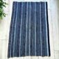 Grey-blue cotton cloth with bands of dark and pale stripes, laid flat on a timber floor beside a plant