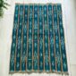 Green-blue cotton cloth with pale diamond motifs, laid flat on a timber floor beside a plant