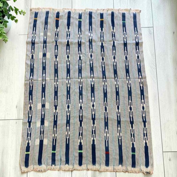 bashiri-indigo-cotton-246-walewale-handwoven-african-textile-main Pale striped cotton cloth with narrow indigo motif columns, laid flat on a timber floor beside a plant