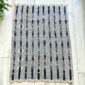 Pale striped cotton cloth with narrow indigo motif columns, laid flat on a timber floor beside a plant