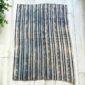 Pale cotton cloth with faded indigo stripes, laid flat on a timber floor beside a plant