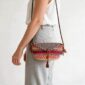Woven mini Bolga shoulder bag in purple and pink elephant grass, worn on the shoulder with a plaited leather strap
