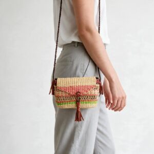 Woven mini Bolga shoulder bag in coral and green elephant grass, worn on the shoulder with a plaited leather strap