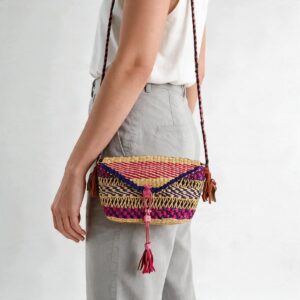 Woven mini Bolga shoulder bag in pink and purple elephant grass, worn on the shoulder with a plaited leather strap