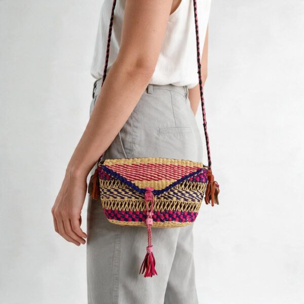 Woven mini Bolga shoulder bag in pink and purple elephant grass, worn on the shoulder with a plaited leather strap