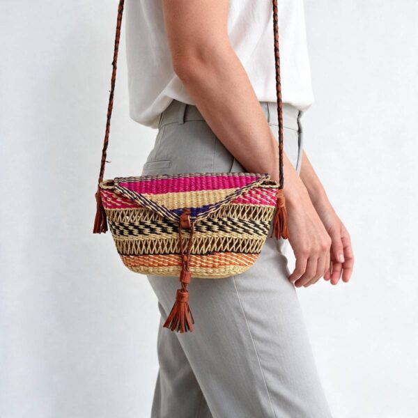 Woven mini Bolga shoulder bag in pink, black, and orange elephant grass, worn on the shoulder with a plaited leather strap
