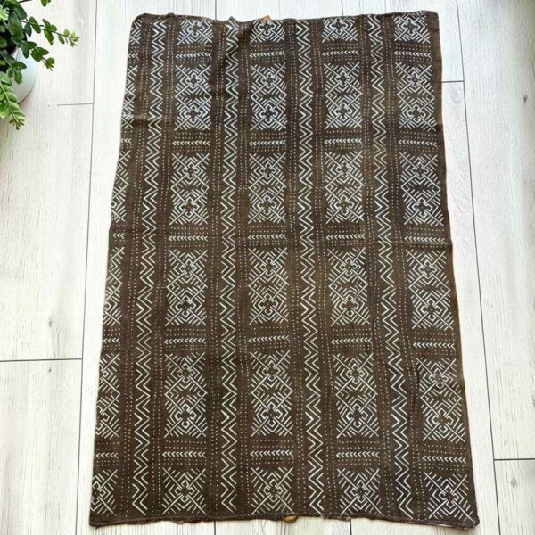 bashiri-mudcloth-medium-160-addax-bogolan-african-fabric-main Medium earth-toned mudcloth with pale zigzag and diamond panels, laid on a timber surface with green leaves
