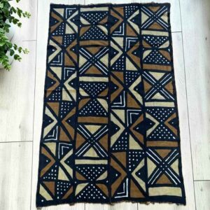 Medium dark mudcloth with large warm-toned triangles and bow-tie shapes, laid on a timber surface with green leaves