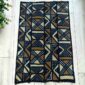 Medium dark mudcloth with large warm-toned triangles and bow-tie shapes, laid on a timber surface with green leaves