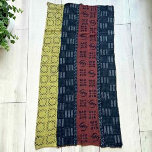 Medium patchwork mudcloth with chevron, dot and flower motifs, laid on a timber surface with green leaves