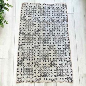 Medium light mudcloth with dark seed shapes and angular lines, laid on a timber surface with green leaves
