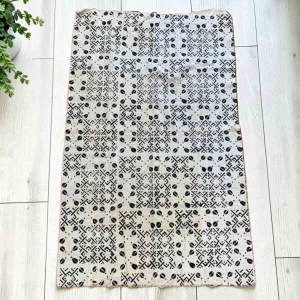 Medium light mudcloth with dark seed shapes and angular lines, laid on a timber surface with green leaves