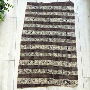 Medium mudcloth in dark and light bands of geometric motifs, laid on a timber surface with green leaves