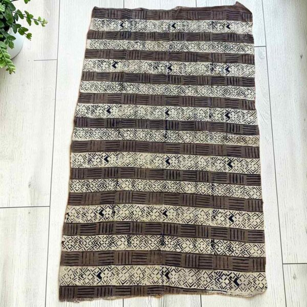 Medium mudcloth in dark and light bands of geometric motifs, laid on a timber surface with green leaves