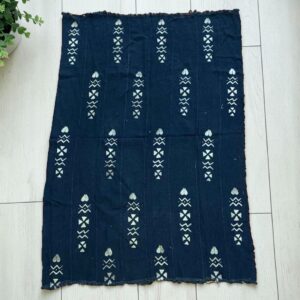 Medium dark mudcloth with columns of pale hearts and arrows, laid on a timber surface with green leaves