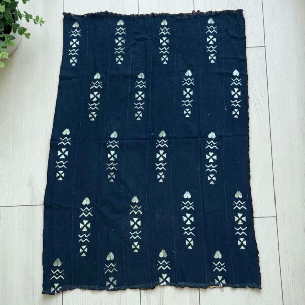 Medium dark mudcloth with columns of pale hearts and arrows, laid on a timber surface with green leaves