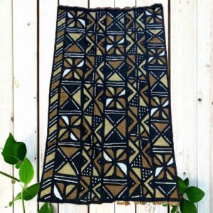 Medium dark mudcloth with a grid of warm-toned and pale triangles, laid on a timber surface with green leaves