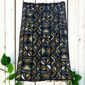 Medium dark mudcloth with a grid of warm-toned and pale triangles, laid on a timber surface with green leaves