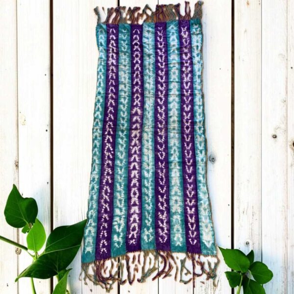 bashiri-mudcloth-small-147-dromedary-african-mud-cloth-fabric-main Small mudcloth with alternating jewel-toned strips and pale chevrons, laid on a timber surface with green leaves