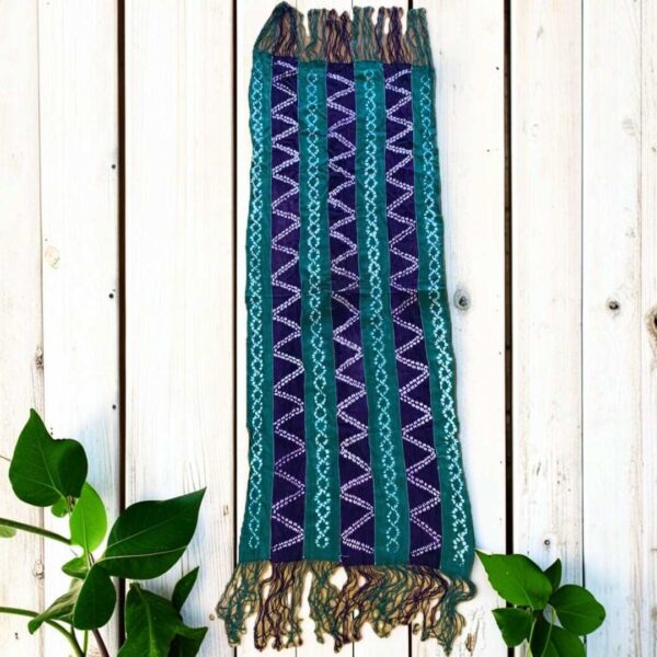 bashiri-mudcloth-small-148-monitor-bogolan-african-textile-main Small mudcloth with jewel-toned strips and pale chain and zigzag patterns, laid on a timber surface with green leaves