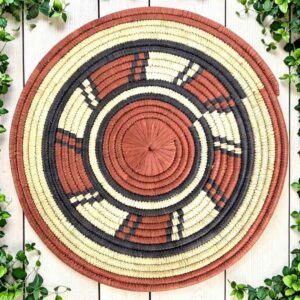 Woven raffia rust, black and natural Burkina platter with a wheel pattern, on white timber with greenery