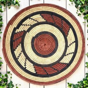 Woven raffia rust, black and natural Burkina platter with a swirl pattern, on white timber with greenery