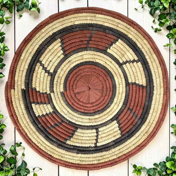 Woven raffia rust, black and natural Burkina platter with a block pattern, on white timber with greenery