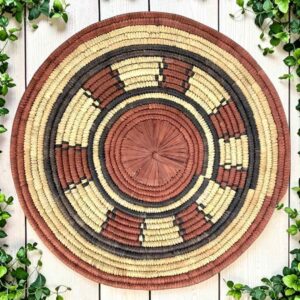 Woven raffia rust, black and natural Burkina platter with a ring pattern, on white timber with greenery