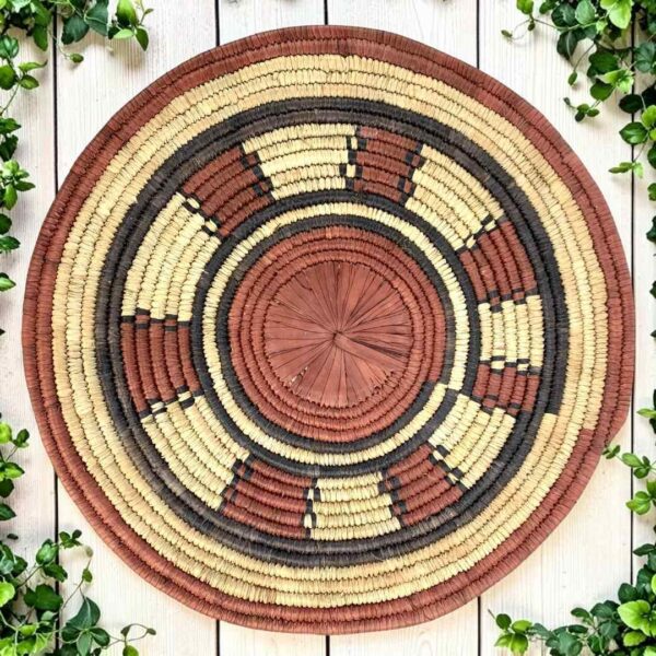 Woven raffia rust, black and natural Burkina platter with a ring pattern, on white timber with greenery