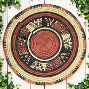 Woven raffia rust, black and natural Burkina platter with a starburst pattern, on white timber with greenery